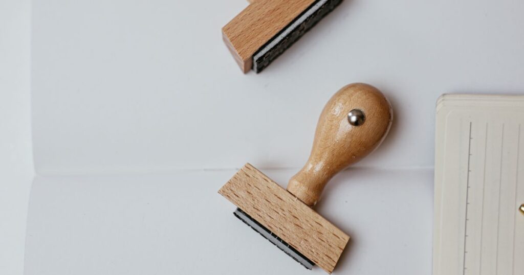 Two unbranded wooden rubber stamps lying on white paper, illustrating the rules on trade mark, patent and registered design claims in Singapore advertising and packaging.