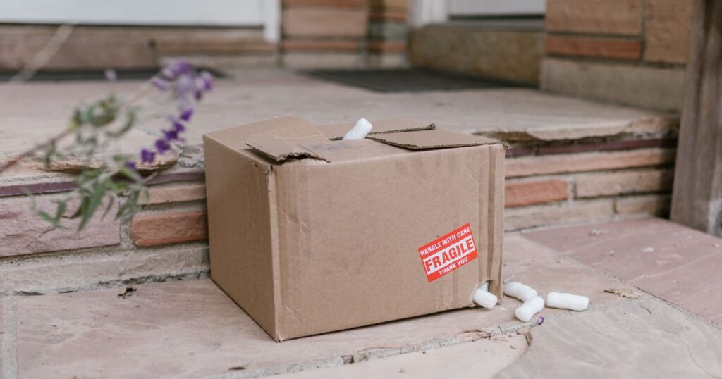 A damaged cardboard parcel with a fragile sticker and spilled packing foam on a doorstep, illustrating consumer rights to refunds and repairs for defective goods bought online in Singapore.