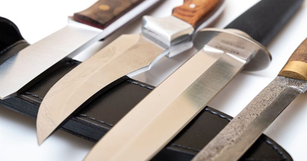 A row of fixed-blade outdoor knives with wooden and rubber handles resting on a black leather sheath, illustrating the rules for listing knives and other regulated items online in Singapore.